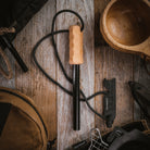 A handcrafted hardwood handle adorns the black stick of the Überleben Kräftig Grip Fire Starter, complemented by a wooden cup on a wood surface.