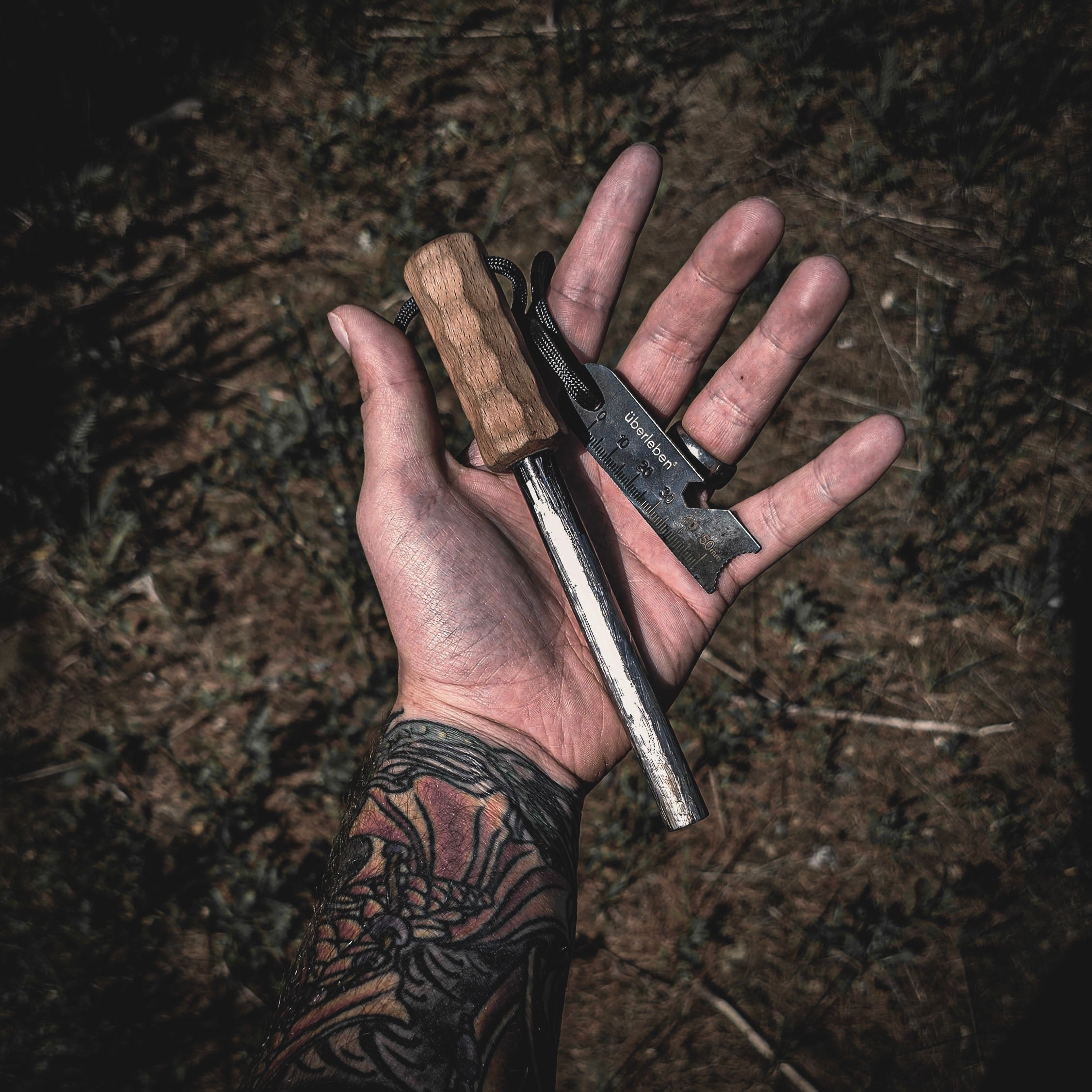 A hand holds the Überleben Kräftig Grip Fire Starter, featuring a handcrafted hardwood handle and a metal striker. This ferro rod is great for bushcraft/survival situations