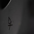 Close-up image of the Überleben Stöker Stove in dark gray, featuring a minimalistic fire icon. The shallow depth of field focuses on the symbol, showcasing the stove's stainless steel craftsmanship.