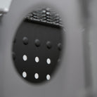 Close-up of the Überleben Stöker Stove. The focus is on the intricately arranged raised and recessed dots on a dark stainless steel surface, framed by an out-of-focus circular opening.