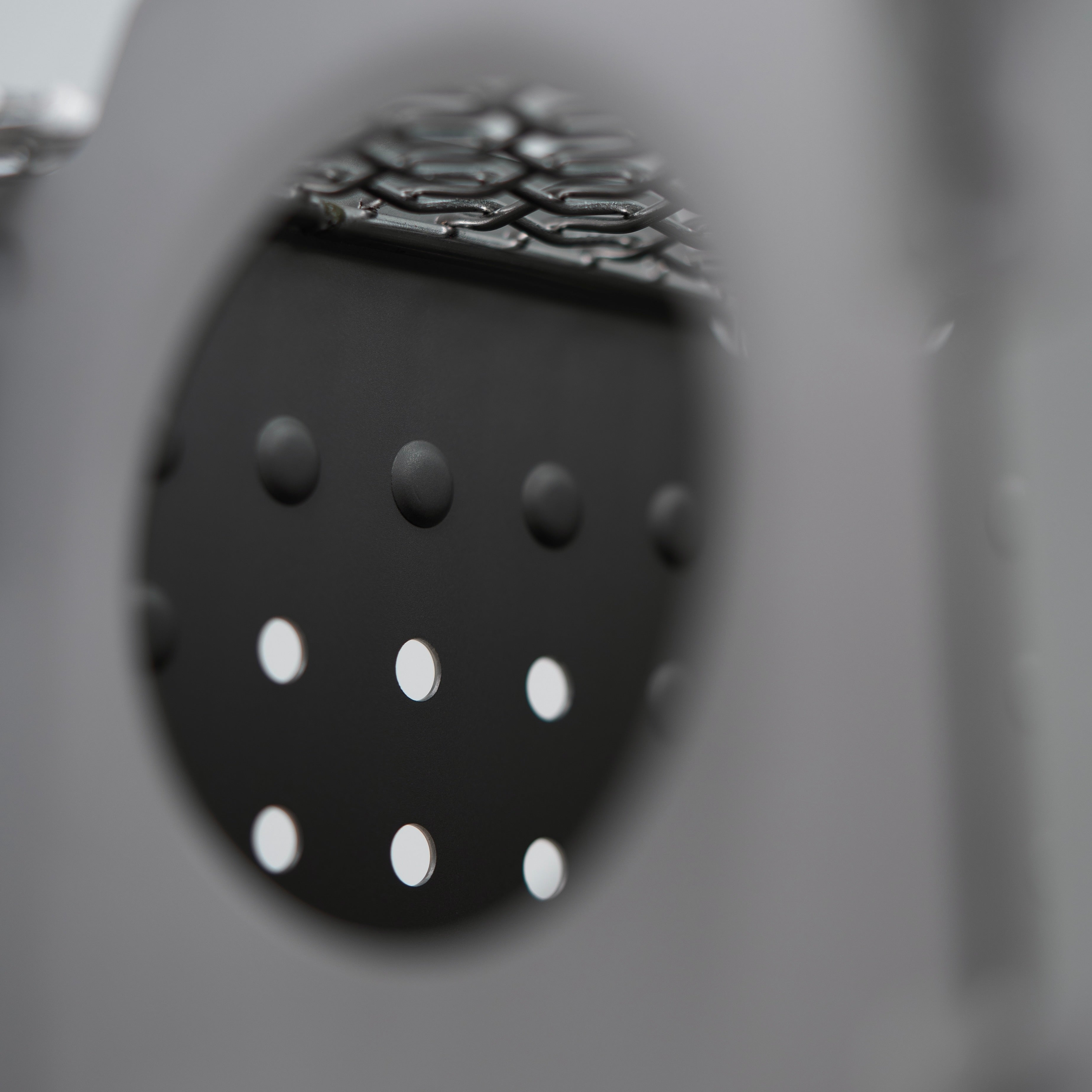 Close-up of the Überleben Stöker Stove. The focus is on the intricately arranged raised and recessed dots on a dark stainless steel surface, framed by an out-of-focus circular opening.