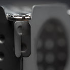 Close-up image of a corner of the Überleben Stöker twig stove, showing the stainless steel grate on a dark-colored, textured surface. The stove has a minimalist design and features a smooth finish, emphasizing an industrial aesthetic.