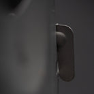 Close-up view of a dark-colored metal tab on a blurred background. The tab is part of the Überleben Stöker Stove, a bushcraft twig stove crafted from stainless steel and partially extended. Distinct focus on its texture and structure, set against a muted, out-of-focus backdrop.