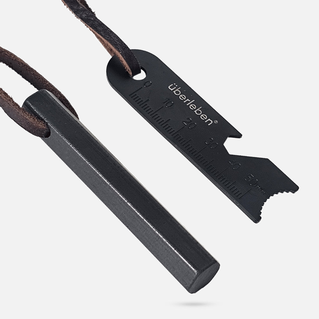 Überleben fire starter, known as the Hexå, featuring a hexagonal shaped ferro rod and a multipurpose striker attached to a leather cord. The striker includes measuring notches and a serrated edge, specifically designed for outdoor and survival use. 