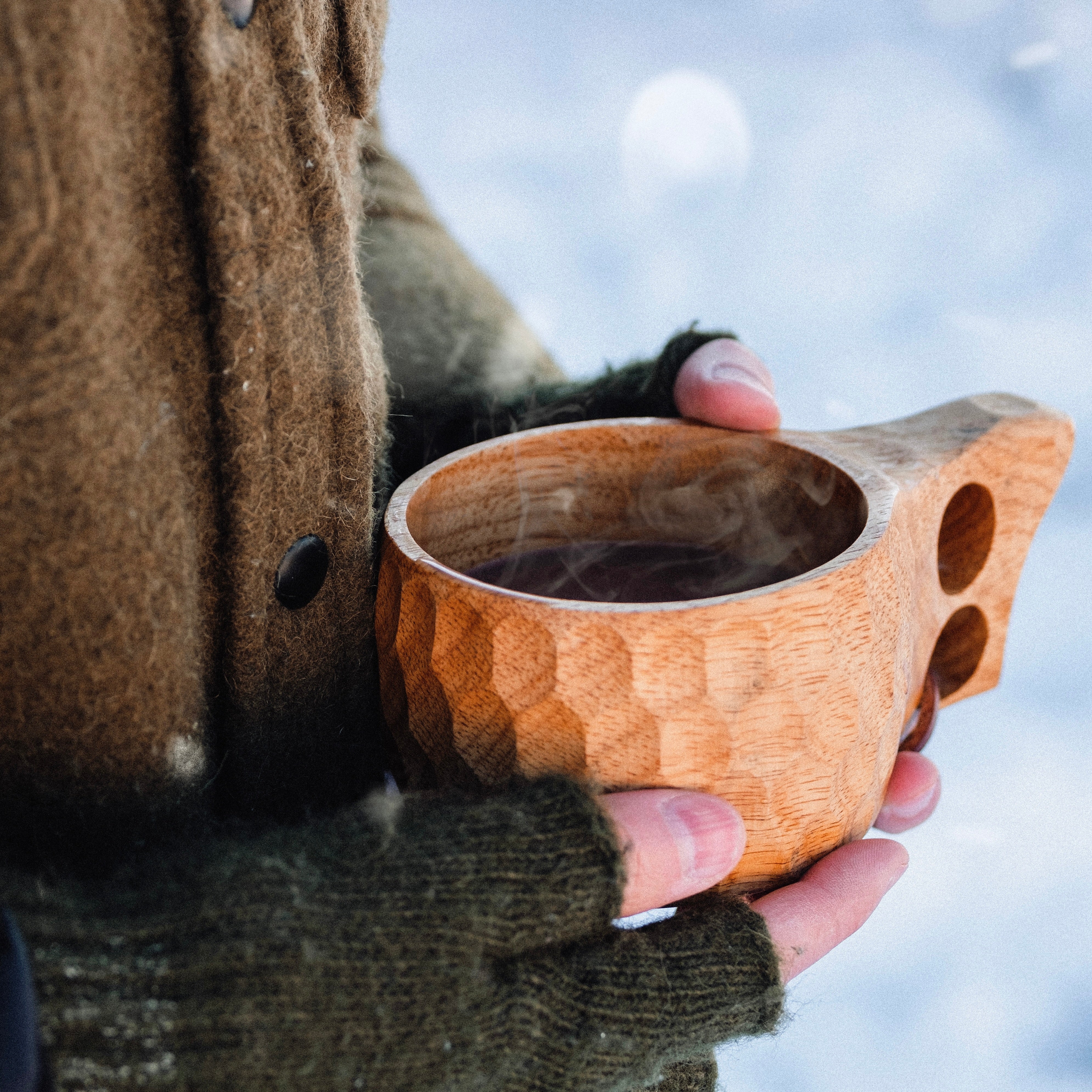 Hands holding an Original 8oz. Kuksa camp cup from Überleben, filled with steaming hot coffee.