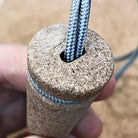 Close-up of a hand holding an Überleben Zünden 2.0 Fire Starter with two gray, braided ropes emerging from a hole in the center of the handle. 