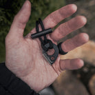 A hand holds a black lanyard with an Überleben Leicht fire starter, complete with a teardrop shaped striker and a short ferro rod.