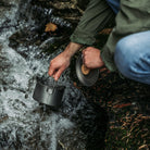 Man using an Überleben bushcraft Titanium Kessel Pot to collect water from a waterfall.