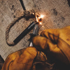 Close-up of a survival fire starter, the Überleben Tindår Wick & Bellow Kit, a paraffin infused hemp rope, being struck to produce a small, bright flame