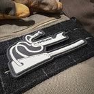 A close-up shot features a black and white Velcro Traddy Patch depicting a stylized drawing of a Zünden ferro rod, with the brand name "Überleben" above it. 